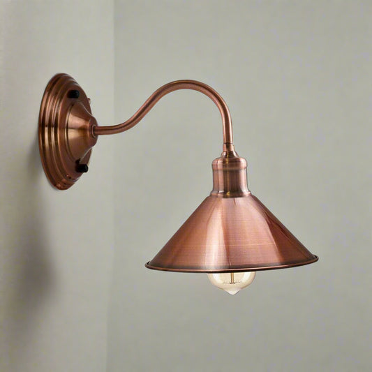 A copper wall-mounted sconce with a cone-shaped lampshade and an exposed bulb, providing a warm light.