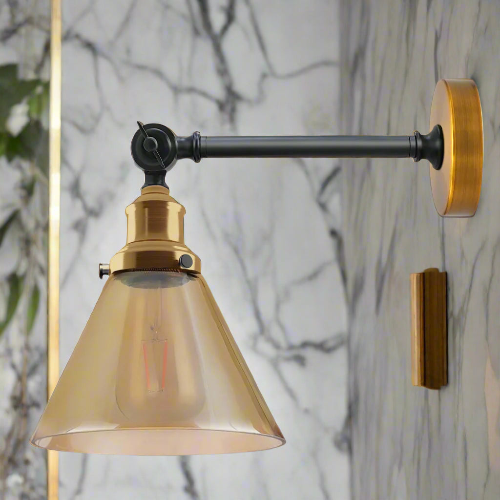A fancy living room wall light featuring a brass-accented adjustable dark arm and a translucent amber cone-shaped shade, mounted on a white marble-patterned wall.