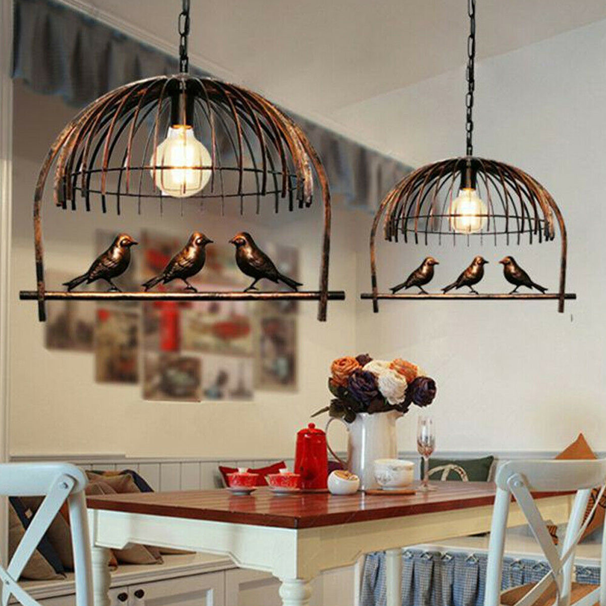 Two antique-style industrial bird cage chandeliers, featuring a dark metal open cage design with perched decorative birds and exposed bulbs, hanging above a rustic dining table setting.
