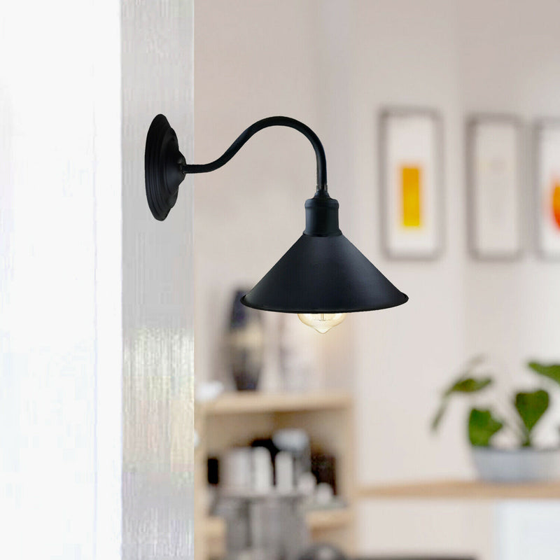 A black metal wall sconce with a conical shade mounted on a wall, with a blurred indoor setting for home decor