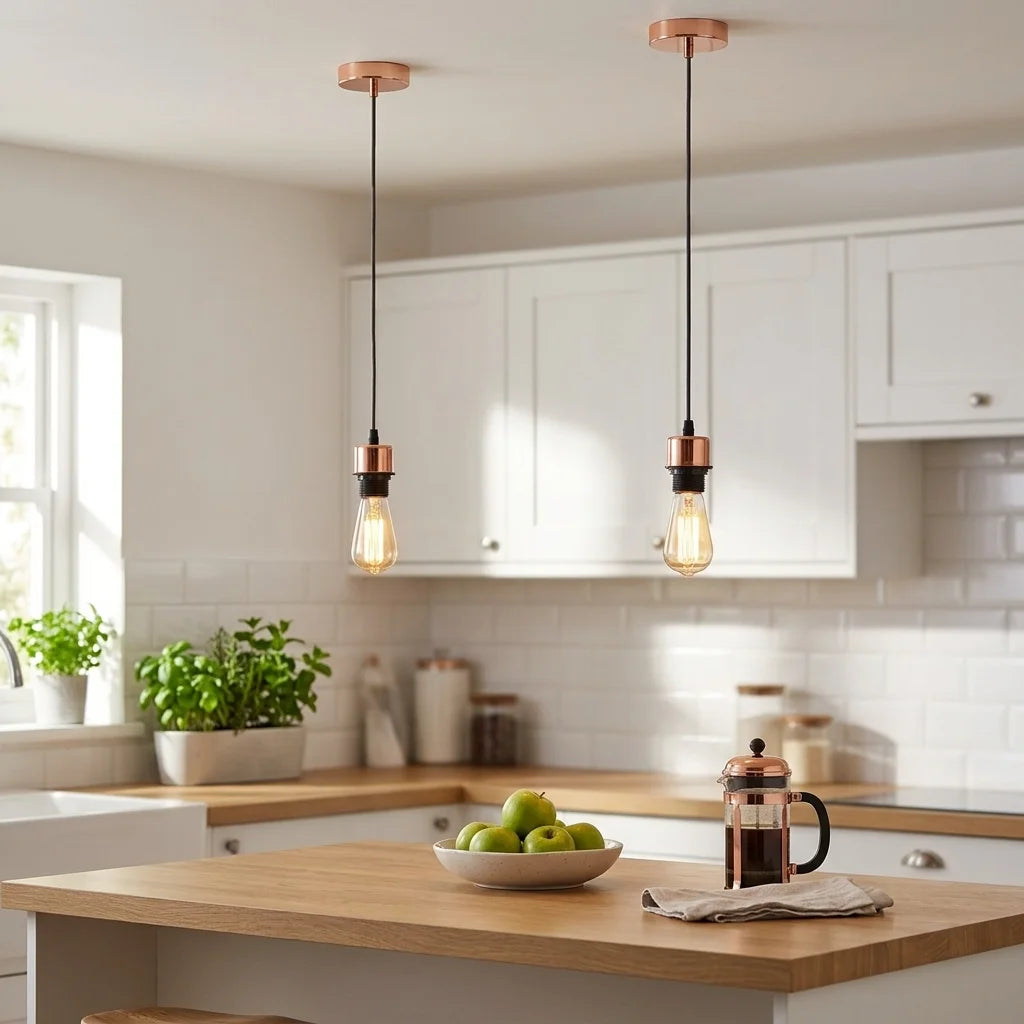 Two copper-finished pendant lights with black cords and exposed Edison-style bulbs hang over a modern kitchen island with a wood countertop, white cabinets, and a tiled backsplash.