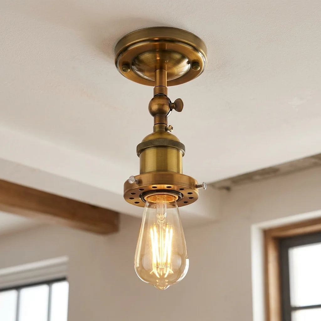 An industrial-style semi-flush mount ceiling light fixture with a warm brass finish and a clear glass bulb, shown installed on a white ceiling in a room.