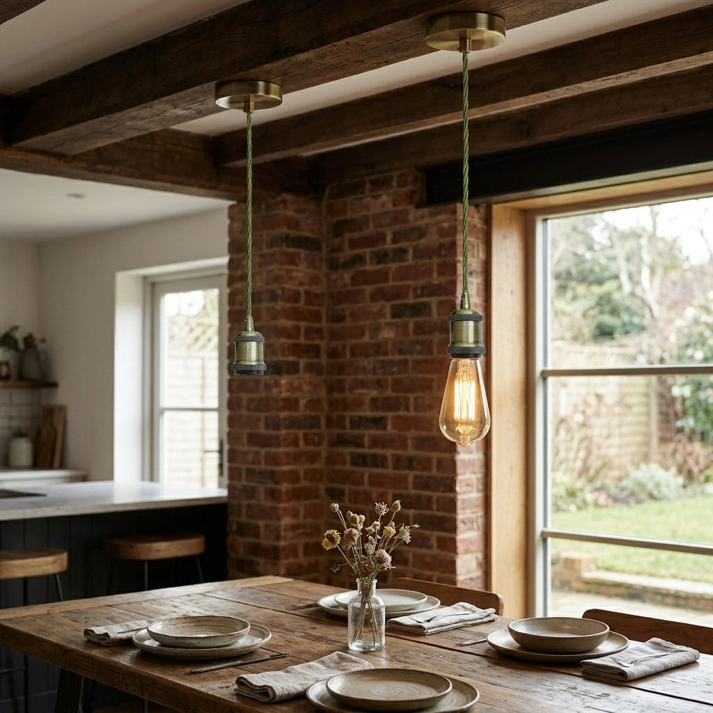 Two industrial-style pendant lights with exposed Edison bulbs hanging over a rustic wooden dining table in a cozy room with brick columns and exposed wooden beams.