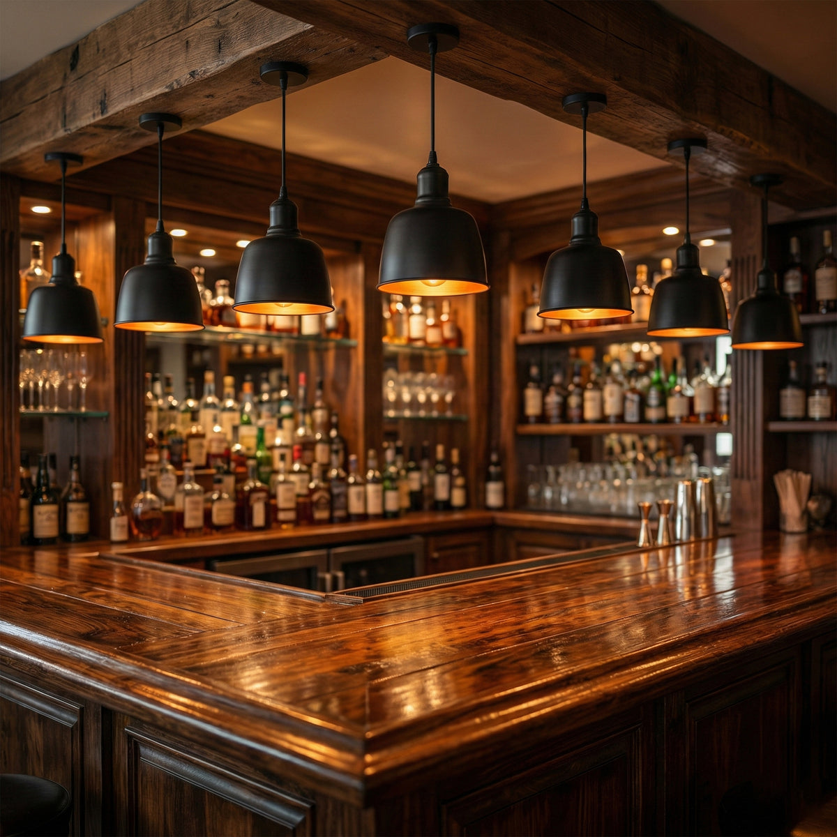 A warm, atmospheric bar interior with a dark wood counter and shelves stocked with bottles. Multiple black dome pendant lights hang above the bar, casting a warm glow.