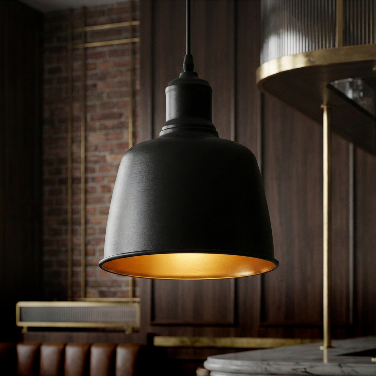 A modern industrial pendant light with a matte black dome shade and a warm gold interior, hanging in a dark wood-paneled room.