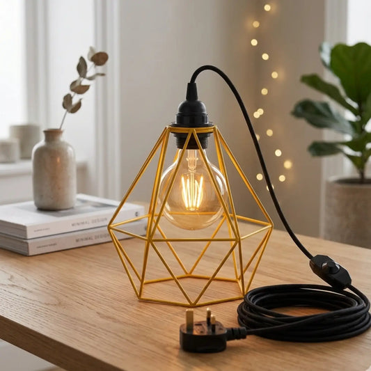 Geometric gold lamp with a lit bulb on a wooden surface, surrounded by decor items.