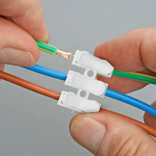 Close-up of a person connecting green, blue, and brown cables into a 3-way push-in wire terminal connector block
