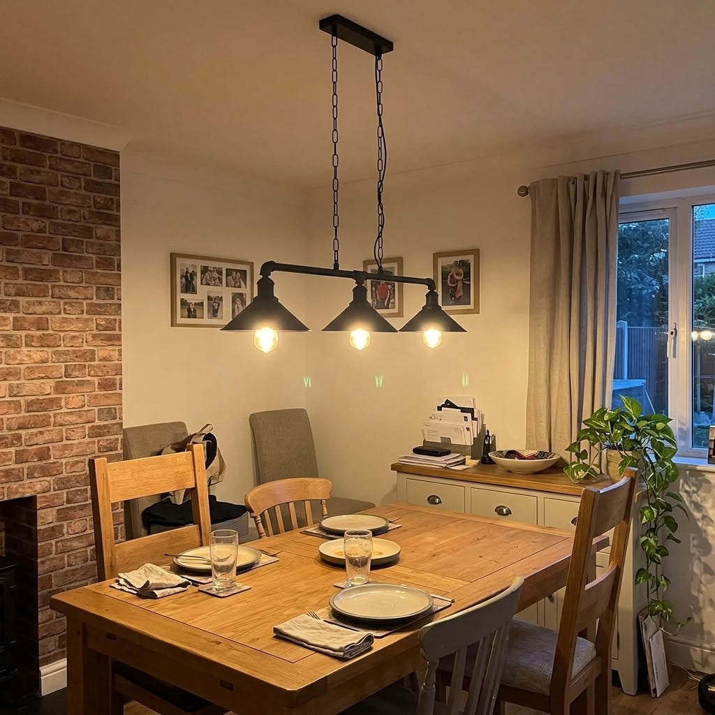 A three-light black metal pendant chandelier with conical shades hangs over a wooden dining table in a cozy home dining room with a brick wall, beige walls, and a window with curtains. Customer review image