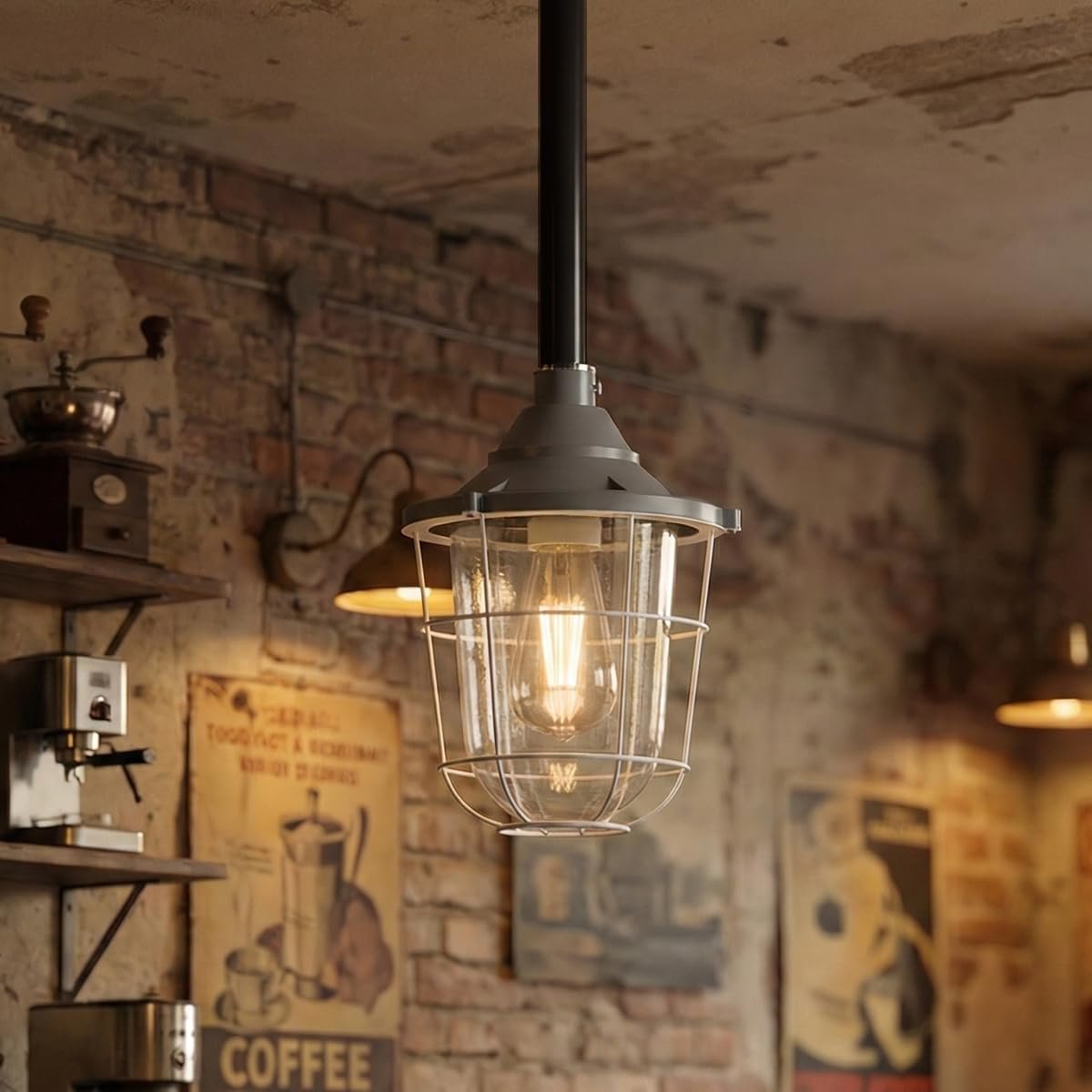 Industrial-style pendant light with a black hanging rod, gray metal top cap, and clear wire cage over a warm glowing Edison bulb, shown in a rustic brick wall cafe interior.