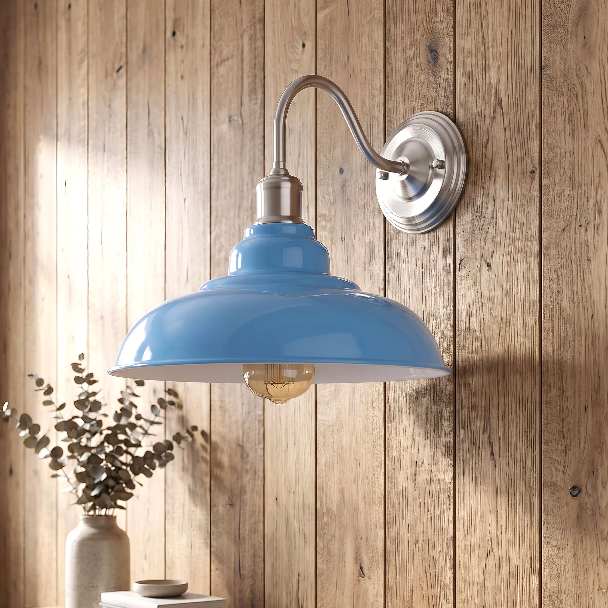 A blue dome-shaped wall sconce with a brushed silver metal arm and backplate, mounted on a rustic wood-paneled wall next to a small vase with dried branches.