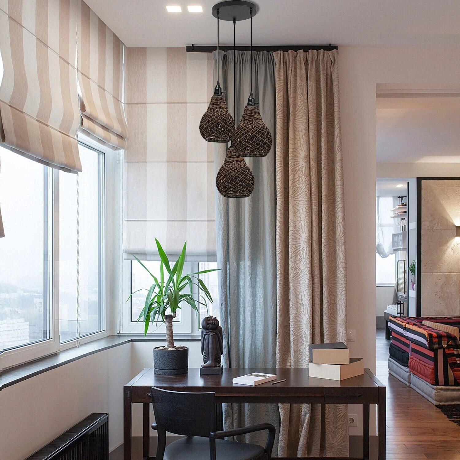 Three vase-shaped rattan wicker ceiling pendant lights hang above a wooden desk in a room with large windows, striped blinds, and patterned curtains.