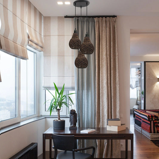 Three vase-shaped rattan wicker ceiling pendant lights hang above a wooden desk in a room with large windows, striped blinds, and patterned curtains.