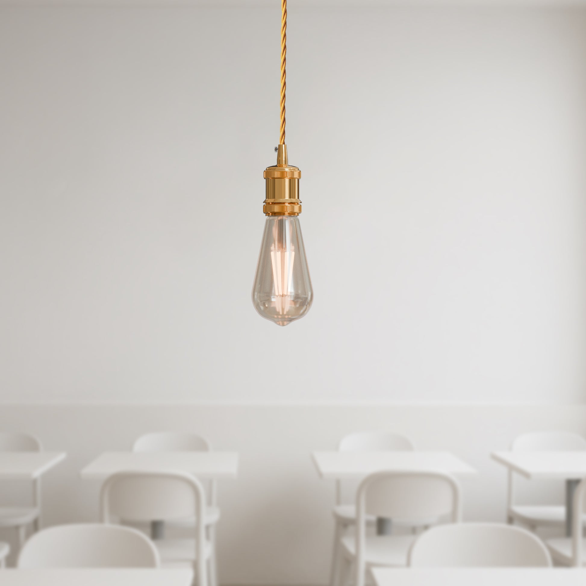 A single French gold pendant light with a twisted fabric cable hanging in a room w
