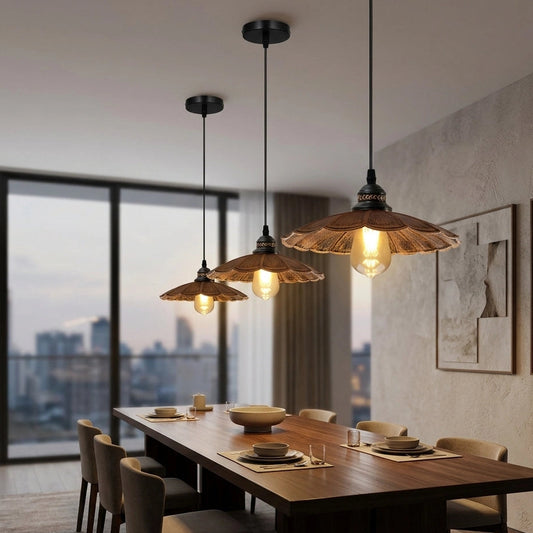 Three rustic pendant lights with bronze metal shades and glowing Edison bulbs hanging over a wooden dining table in a modern, sunlit room with a city view.